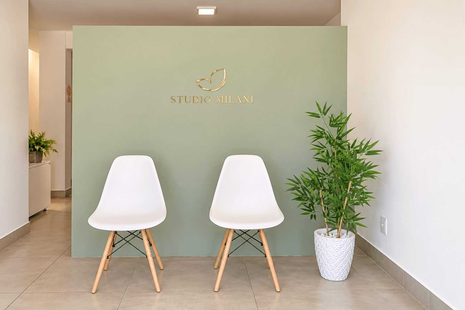 Recepção do Studio Milani: parede verde-sálvia com a logo dourada, duas cadeiras brancas e uma planta